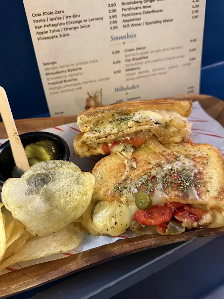 Grilled toastie halves on a wooden board with crisps and pickles