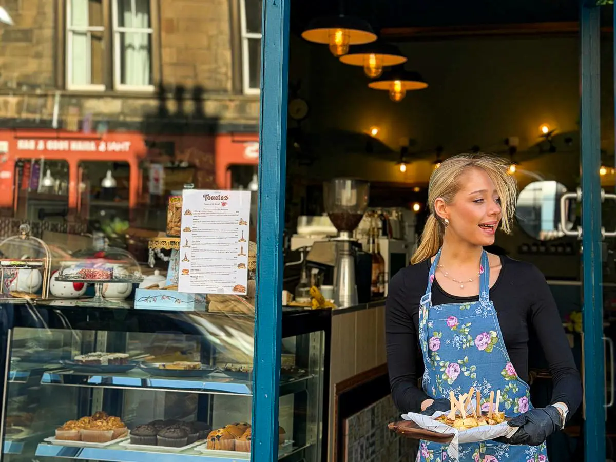 A smiling team member in the glowing doorway of Toastea, holding a board of toasties